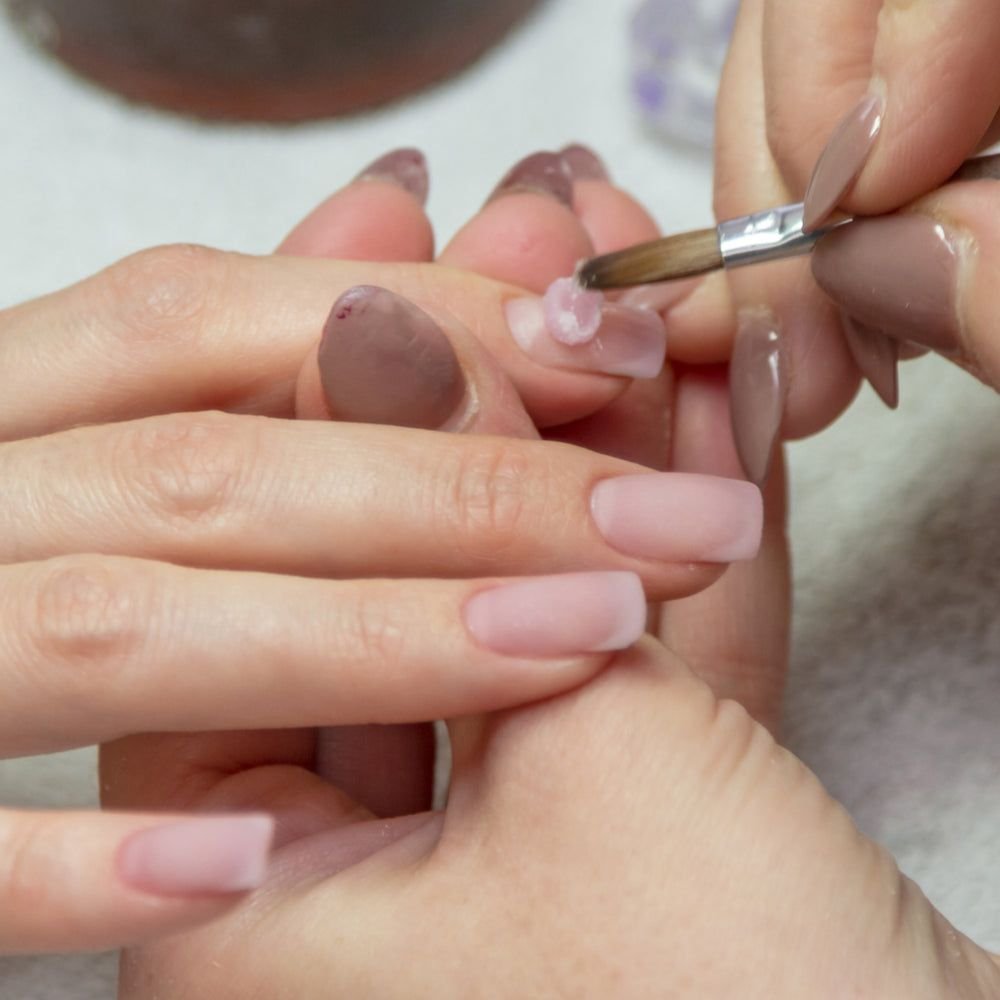 "nail technician applying acrylic mixture during acrylic nails refill process"