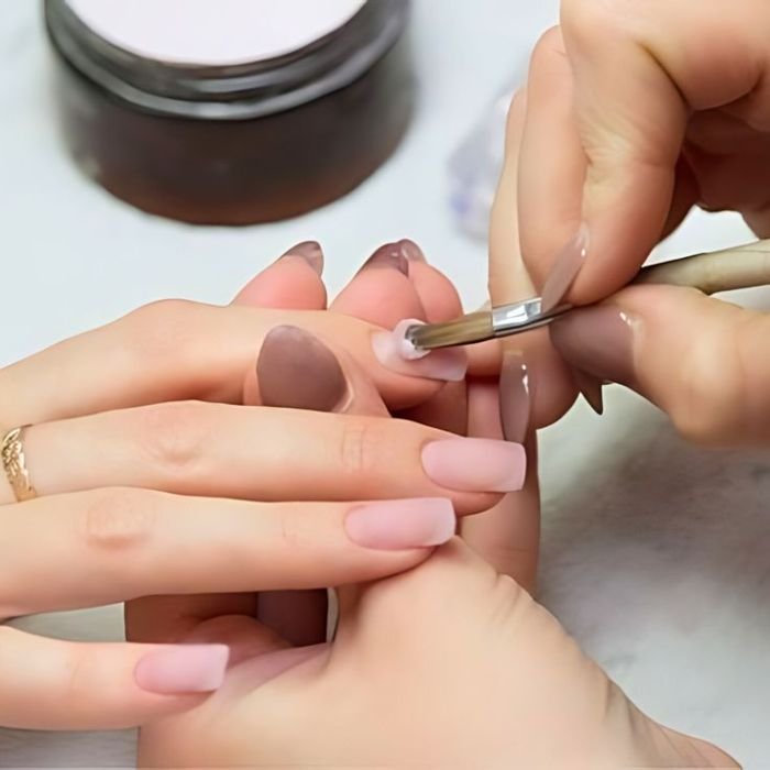Nail technician applying acrylic powder and liquid monomer to create acrylic nails